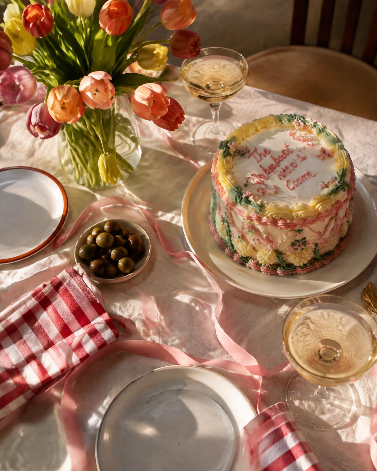 A styled party table with cake, tulips and champagne